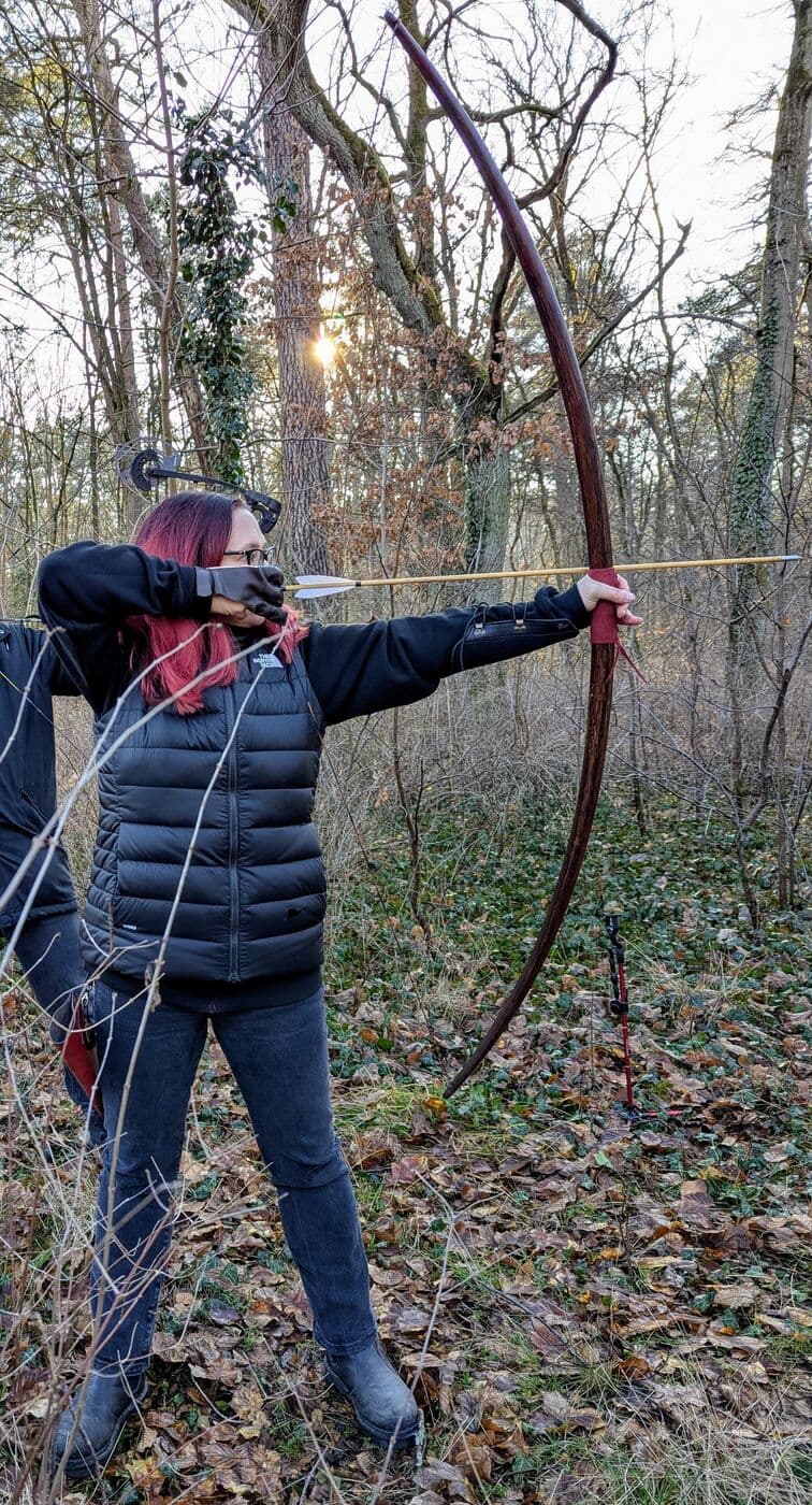 Bogenschützin mit rotem Haar zieht den Bogen im winterlichen Wald aus